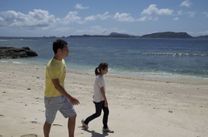 綺麗な海辺の砂浜を歩く山本哲司さんと奥様の写真