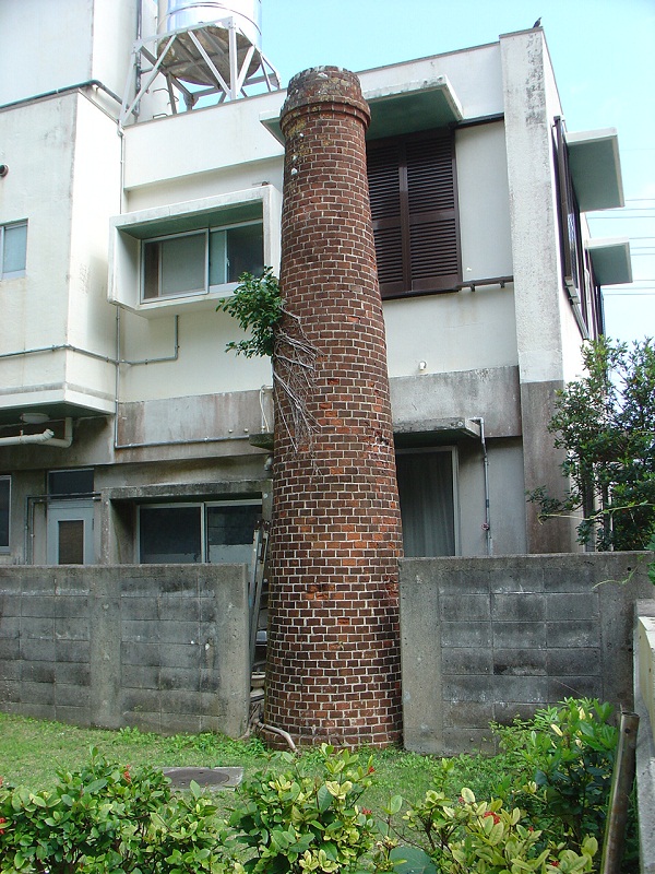 古ぼけたトタンぶきの鰹節乾燥小屋に1本のレンガ造りの煙突が立っている写真